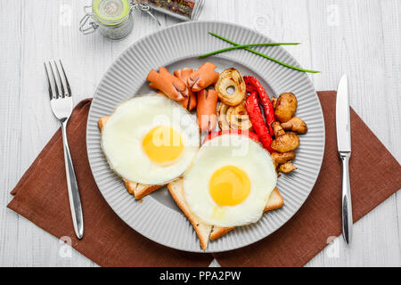 Set for breakfast fried eggs, grilled vegetables, sausages. Bread on a wooden table. Stock Photo