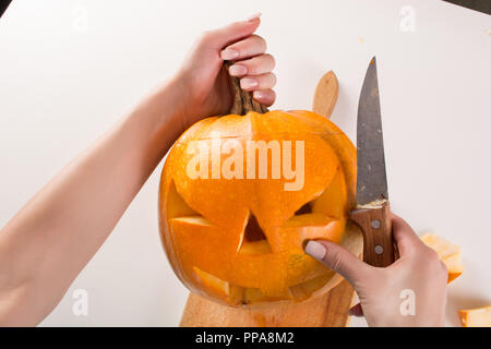 Preparing pumpkin for Halloween holiday on kitchen board and knife in woman hand. Close up, selective focus Stock Photo