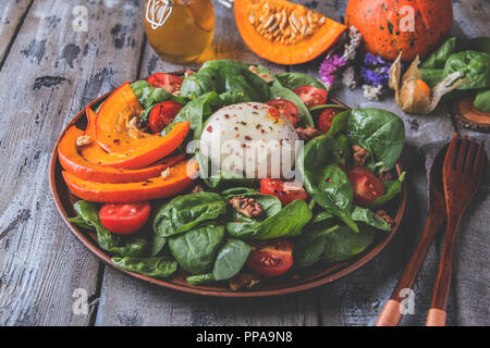 salad with baked pumpkin, mozzarella cheese, spinach greens, tomatoes in a plate on a wooden table Stock Photo