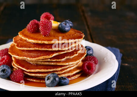 Stack of pancakes with berries and maple syrup on dish