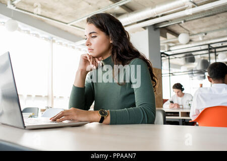 Portrait of pensive young woman using laptop while working in open office, copy space Stock Photo