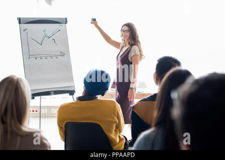 Portrait of modern young woman giving presentation in office and holding camera while smiling at audience, copy space Stock Photo