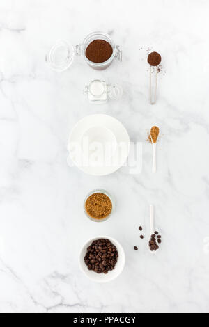Coffee beans, ground coffee, brown and white sugar, coffee measuring spoon and an empty coffee cup on white marble background. Stock Photo