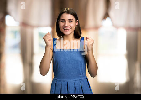 Young excited woman on blurred background. Portrait of happy ecstatic winning girl clenched fists hand celebrating the victory. Stock Photo