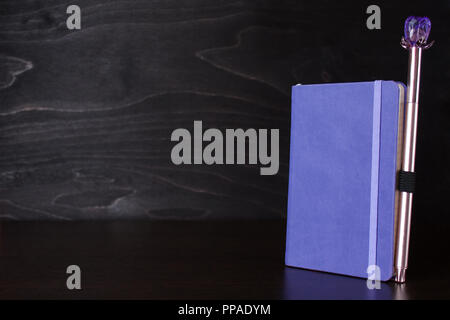 Purple notepad with an attached pen on the table on a black woodenl background Stock Photo