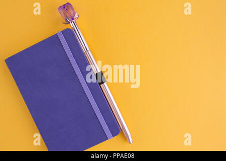 Purple notebook with pen on a yellow background Stock Photo