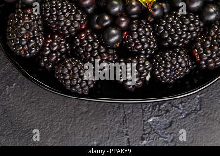 Photo on top of blackberries, black currant on black plate on black empty background Stock Photo