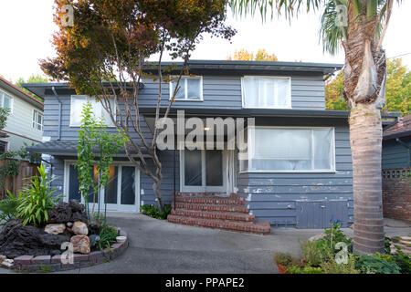 View of back of grey house with sliding glass doors and window covered in plastic and repairs to cracked peeling wood siding with primer preparing for Stock Photo