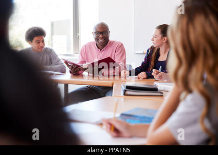 Male High School Tutor Sitting With Students At Desk In Class Stock Photo