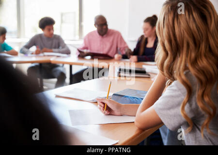 Female High School Student Writing Notes Whilst Sitting At Desk In Class Stock Photo