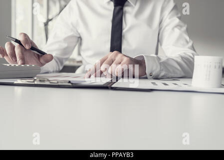 Retro toned image of business person checking facts on various printed paper charts with calculator and pen.