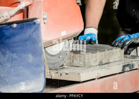 Building contractor using an angle grinder to cut a paving stone. Stock Photo