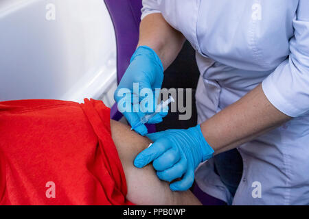 Doctor in blue gloves akes vaccination in the shoulder of patient in a hospital. Prophylaxis and treatment of infectious and viral diseases. Inoculation against influenza. Vaccination against rabies. Stock Photo