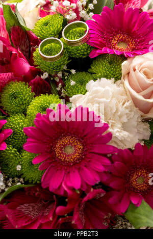 Two wedding rings on the scented and delicate flowers of a bridal colorful bouquet with purple daisies, white carnations and pale pink roses. Stock Photo