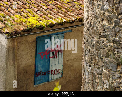 pattern of red graffiti on blue and white window shutters on rendered building with green tiled roof behind Seix castle in the Ariège Pyrénées, France Stock Photo
