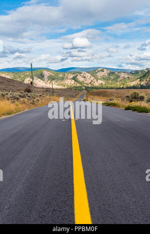 Highway through rolling grasslands disappearing into distant mountains Stock Photo