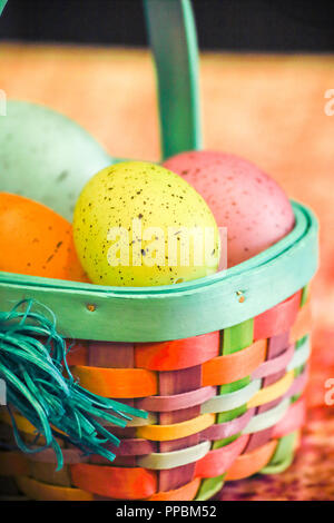 Colorful easter eggs in easter basket vertical over orange background. Stock Photo