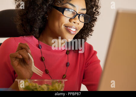 Millennial  businesswoman having lunch while looking at computer Stock Photo