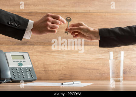 Businesswoman handing over a house key to a businessman in a conceptual image with their arms reaching across a desk with telephone and wooden backgro Stock Photo