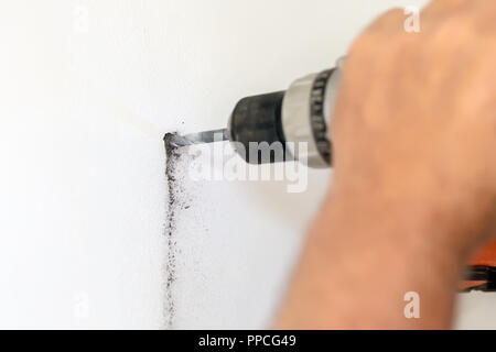 Close-up man holding power drill in hand and making hole in white wall. DIY. House building repair and renovation Stock Photo