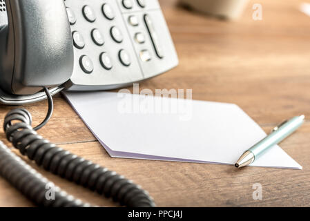 Pen lying on blank white note cards next to a landline telephone on a wooden office desk. Copy space ready for your notes or text. Stock Photo
