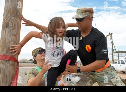 Sgt. Marcel Lopes-Gines, 210th Readiness Support Group, Aguadilla, Puerto Rico, and Capt. Vivian Redeye, 7251st Medical Support Unit, Albuquerque, N.M., assist a child in climbing overhead bars at the Air Assault Obstacle Course during the third annual Community Outreach Day at Fort Bliss Aug. 25. This year’s event was coordinated by the 210th RSG and the 1st Armored Division Iron Training Detachment - along with volunteers of Child Crisis Center, Big Brothers Big Sisters, and the El Paso Police Department – to mentor and interact with citizens of El Paso, Texas. Stock Photo