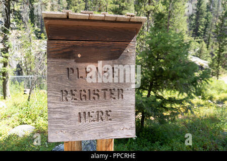 Sign post in an Idaho forest requires hikers and campers to register here - Please Register Here - for safety Stock Photo