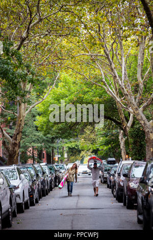 Couple carrying paddleboards in middle of street between rows of parked cars, New York City, New York, USA Stock Photo