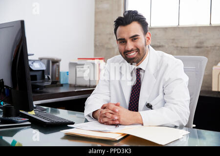 Smiling Hispanic male doctor sitting at desk, portrait Stock Photo