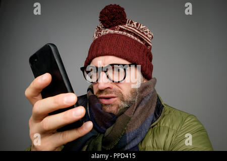 Funny man in glasses anf warm clothes typing sms on gray background Stock Photo