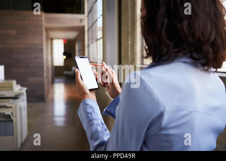 Young businesswoman using smartphone in office, back view Stock Photo