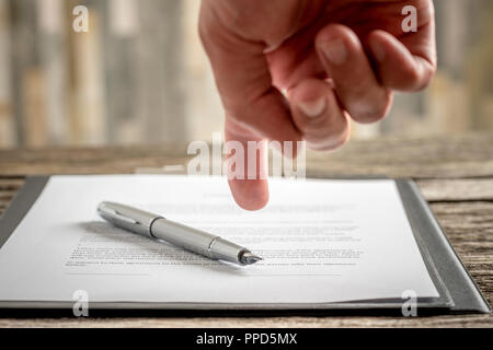 Man pointing his finger to a typed document with a pen lying on top of it as he requests signature, close up view of his hand and paperwork. Stock Photo