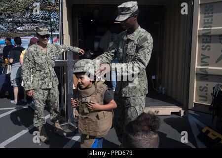 ANGELES (Sept. 2, 2018) Equipment Operator Constructionman Tyrell Puryear, attached to Construction Battalion Maintenance Unit 303, helps a child try on a Kevlar helmet during a military display and demo at the Battleship Iowa Museum during Los Angeles Fleet Week (LAFW). LAFW is an opportunity for the American public to meet their Navy, Marine Corps and Coast Guard teams and experience America's sea services. During fleet week, service members participate in various community service events, showcase capabilities and equipment to the community, and enjoy the hospitality of Los Angeles and its  Stock Photo