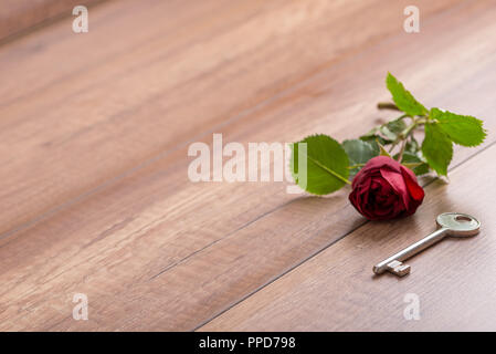 Single Romantic Red Long Stemmed Rose Lying on Wooden Surface with Copy Space Next to Old Fashioned Brass Key. Stock Photo