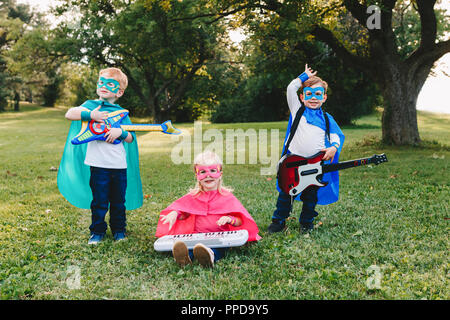 Cute adorable preschool Caucasian children playing superheroes music band rock group. Three kids friends having fun together outdoors in park. Happy a Stock Photo