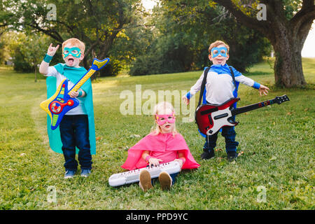 Cute adorable preschool Caucasian children playing superheroes music band rock group. Three kids friends having fun together outdoors in park. Happy a Stock Photo