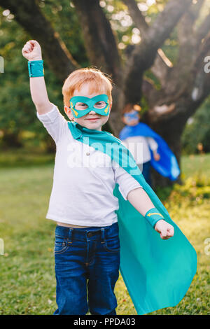 Cute adorable preschool Caucasian child playing superhero in costume. Boy kid wearing green mask and cape having fun outdoors in park. Happy active ch Stock Photo