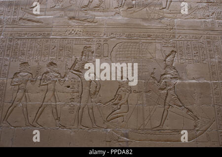 Egypt. Edfu. Temple of Horus. 3rd century B.C. Relief depicting the god Horus standing on a boat and avenging his fatherÕs murder in a battle with his Uncle, the god Seth, depicted in the form of  an hippopotamus underneath. Horus, standing, and Isis, kneeing, in a ship with a sail capturing the Hippo. Stock Photo