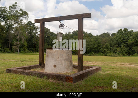 An old tin bucket tied to a rope going through a pulley sits ready to retrieve well water Stock Photo
