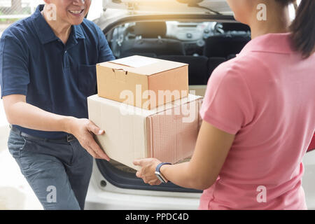 Woman receiving parcel cardboard box from delivery man Carrying Courier Shipping Mail from making an online order while standing in front of the house Stock Photo