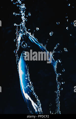 Dynamic splash of water on a dark background. Flying transparent liquid with a shiny surface. High-speed explosion photography. Stock Photo