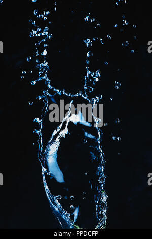 Dynamic splash of water on a dark background. Flying transparent liquid with a shiny surface. High-speed explosion photography. Stock Photo