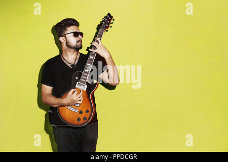 Closeup of a handsome passionate expressive cool young brunette rock musician men playing electric guitar standing against Yellow background Stock Photo