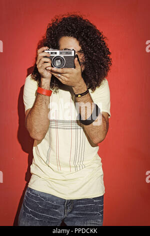 Closeup of one handsome passionate expressive cool young brunette photographer men with long curly hair holding a vintage SLR camera standing against  Stock Photo