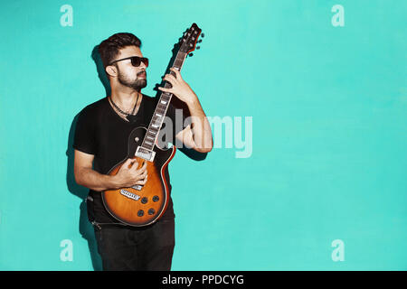 Closeup of one handsome passionate expressive cool young brunette rock musician men playing electric guitar standing against Blue background Stock Photo