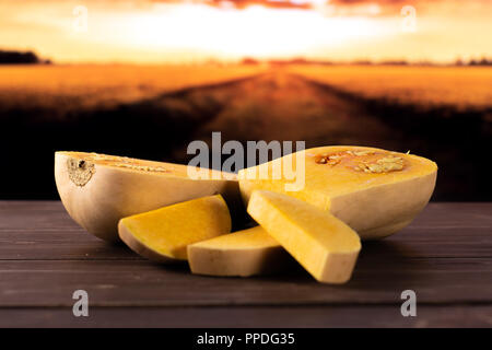 Group of two halves three slices of smooth pear shaped orange butternut squash waltham variety with autumn field and sunset in background Stock Photo