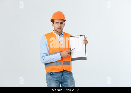 Frustrated young engineer with hardhat and reflective vest checking on mistake in document over gray background Stock Photo
