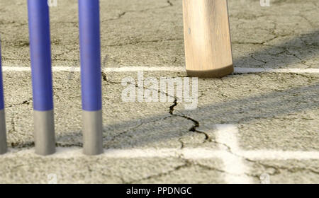 A tip of a cricket bat sliding over the crease on a cracked grass pitch background - 3D render Stock Photo