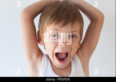 happy shouting little caucasian boy in white shirt with hands behind his head Stock Photo