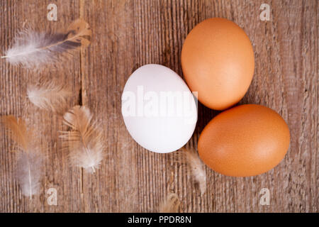 three eggs and feathers on rustic wooden table Stock Photo